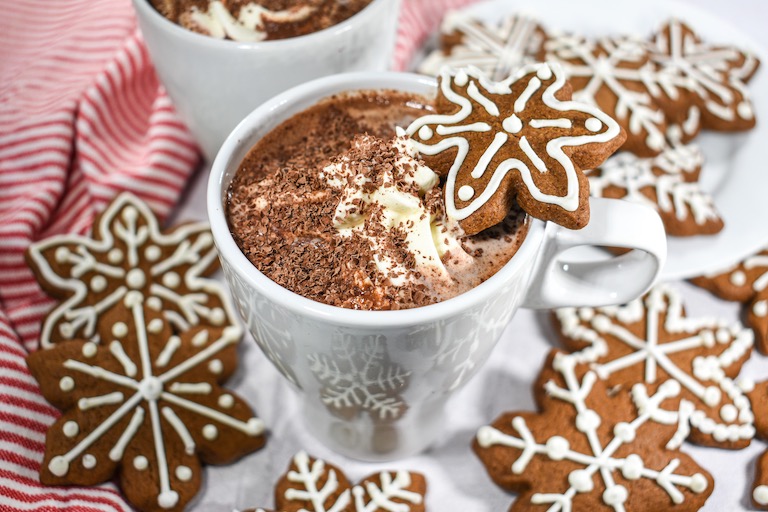 A mug of gingerbread hot chocolate surrounded by snowflake shaped gingerbread cookies