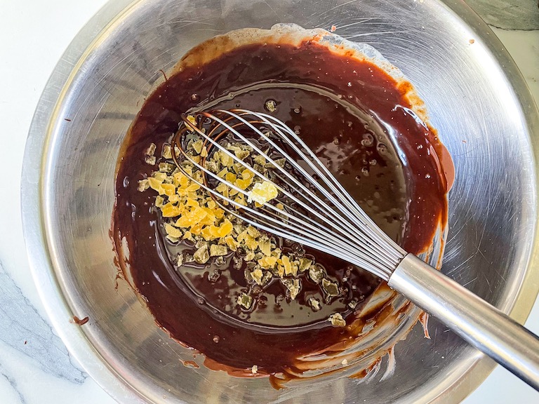 Chopped candied ginger and a whisk in a bowl of chocolate ganache