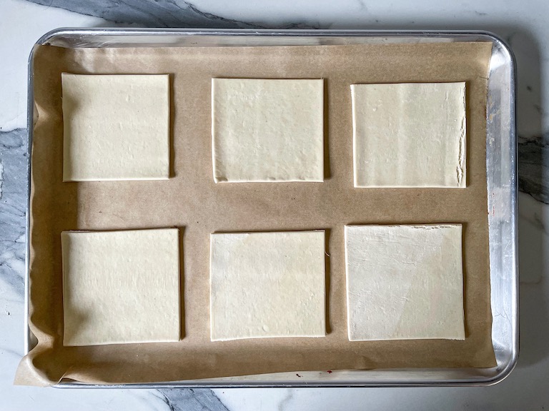 A parchment lined tray with squares of puff pastry