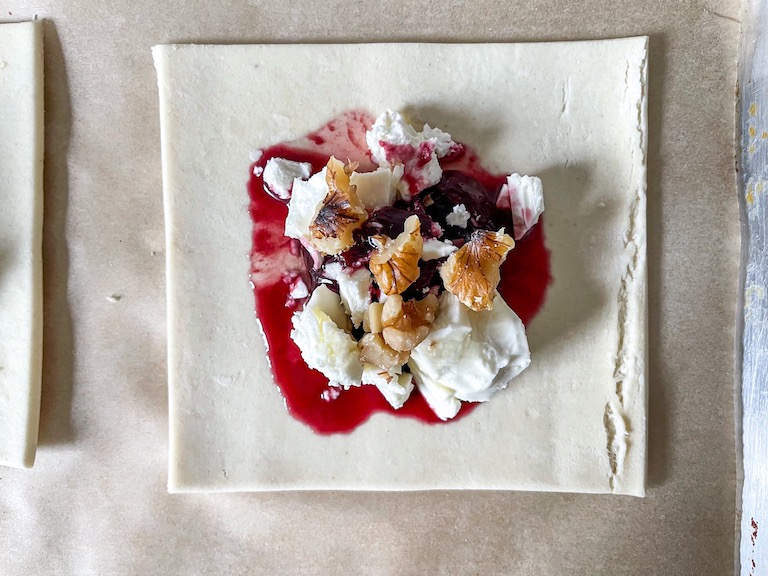 Closeup of a square of puff pastry with cherry compote, feta, and walnuts