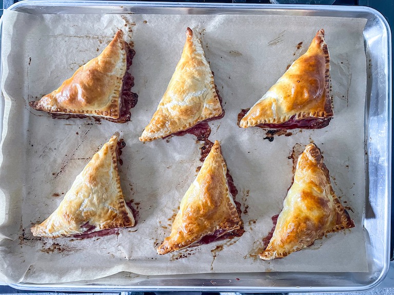 A tray of puff pastry triangles with cherries and feta