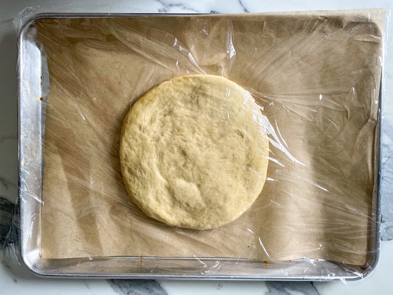 Focaccia dough on a tray covered in plastic wrap