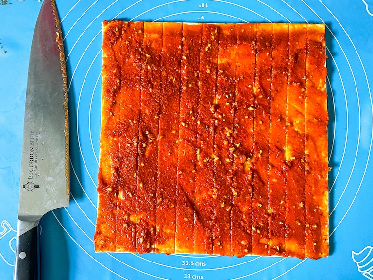 Slices of puff pastry with red pesto, and a knife