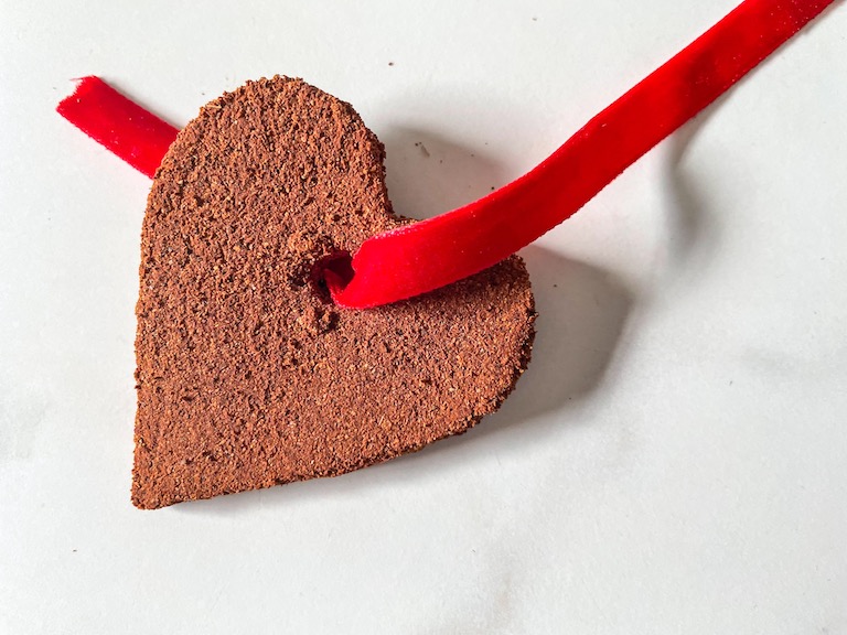 Red ribbon threaded through a heart shaped cinnamon ornament