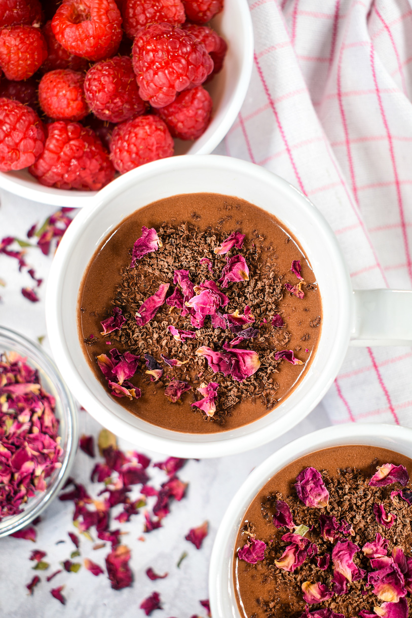 Looking down into two mugs of raspberry and rose hot chocolate, next to a dish of fresh berries