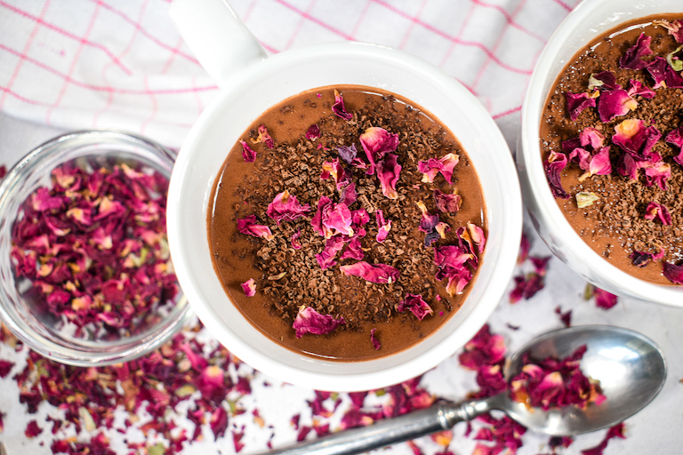 Two mugs of rose hot chocolate with a dish of dried rose petals and a spoon