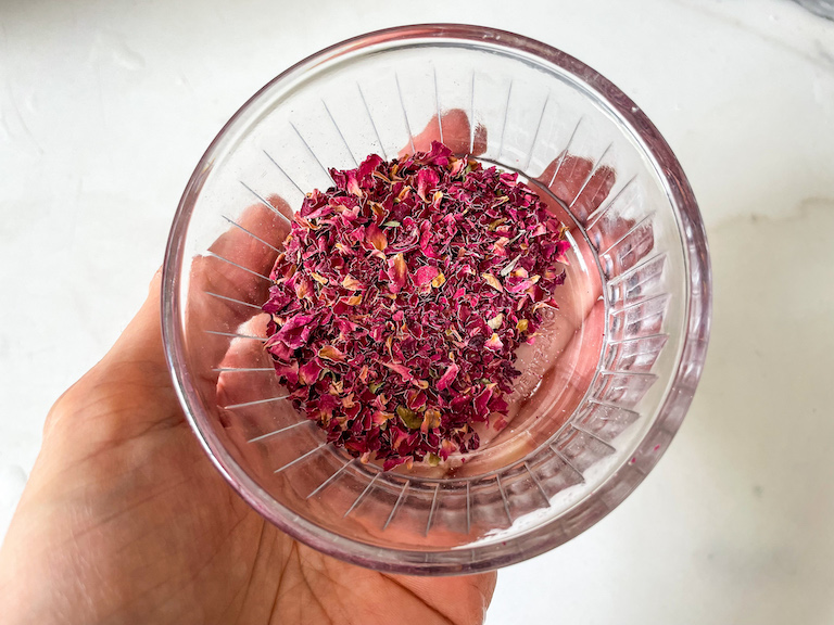 Hand holding a bowl of ground rose petals