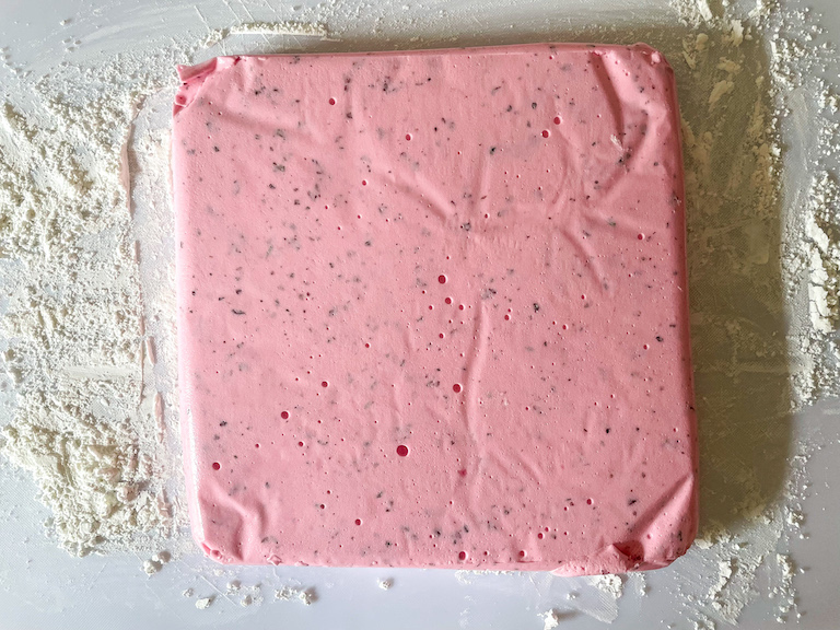 Pink marshmallow slab on a dusted cutting board