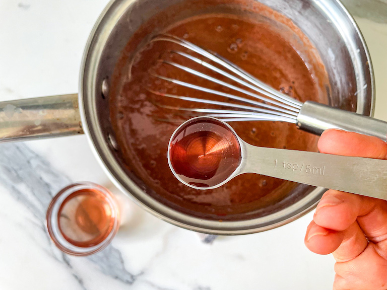 Hand holding a teaspoon of rosewater