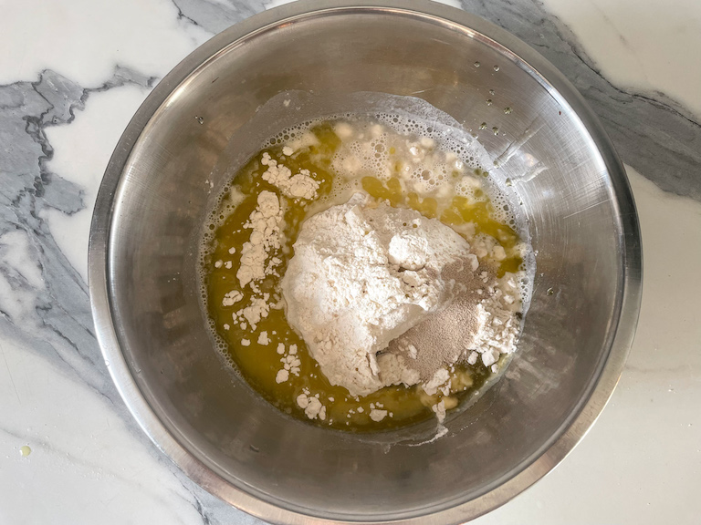 A bowl with flour, yeast, water, and oil