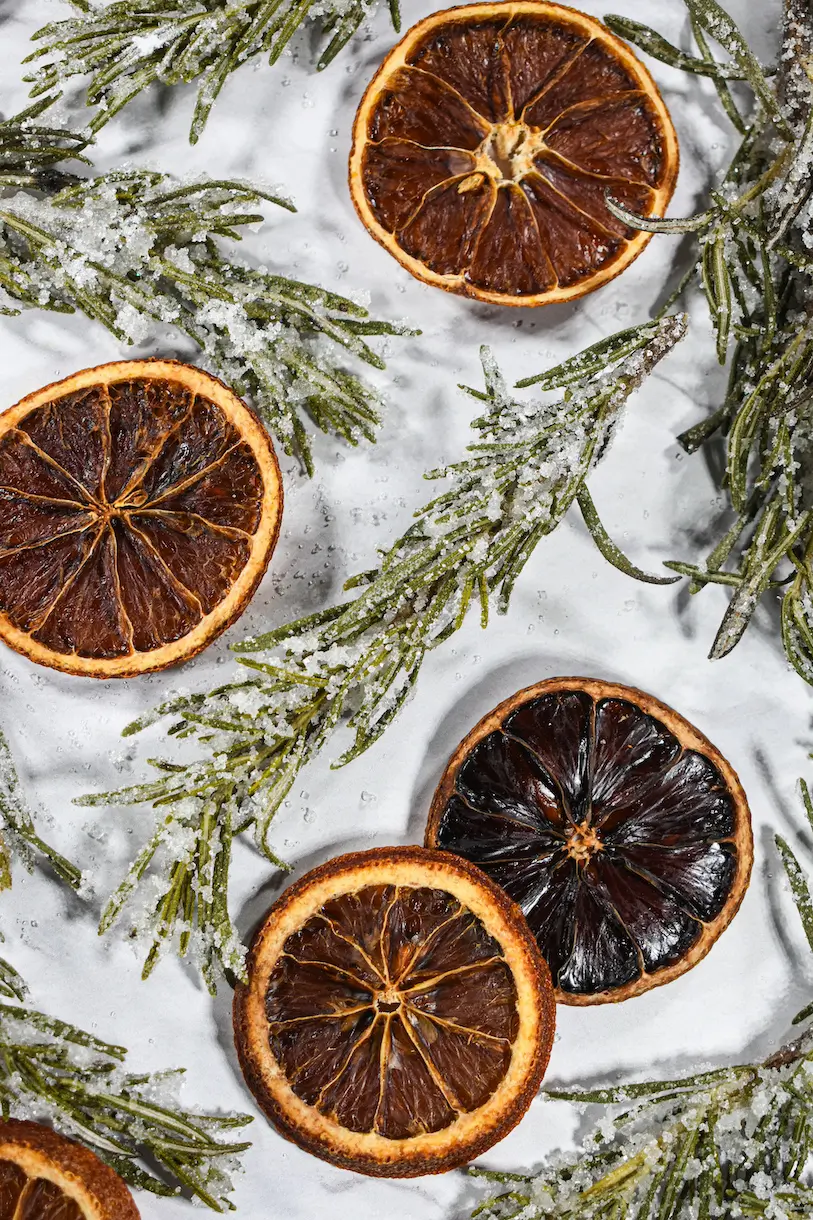 Sugared rosemary and orange slices on a white surface