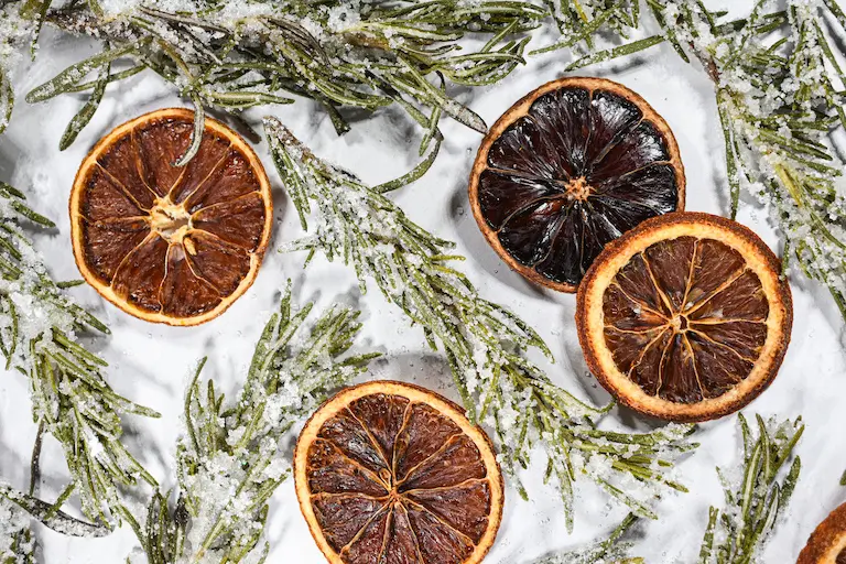 Sugared rosemary and orange slices on a white surface