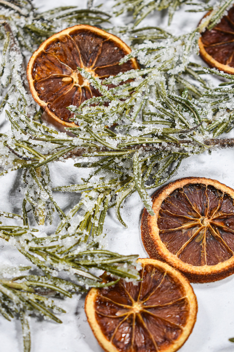 Sugared rosemary and orange slices on a white surface