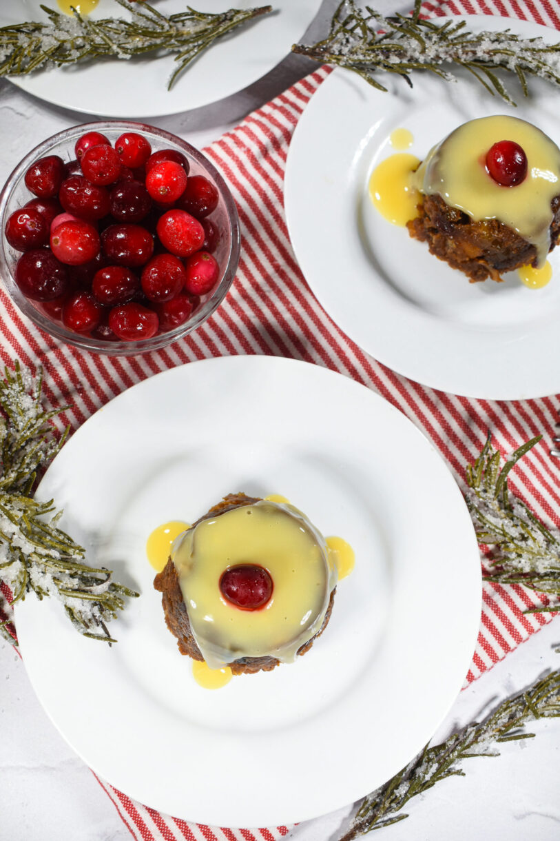 Christmas puddings, cranberries, sugared rosemary, and a striped tea towel on a white surface