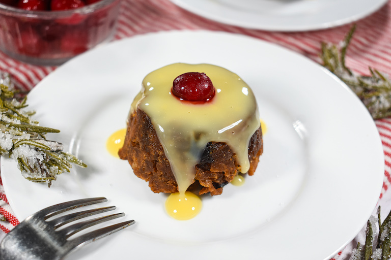 A Christmas pudding on a plate with cranberry and custard