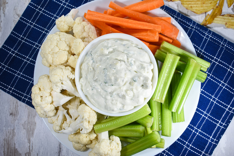 A bowl of blue cheese dip on a plate surrounded by sliced vegetables