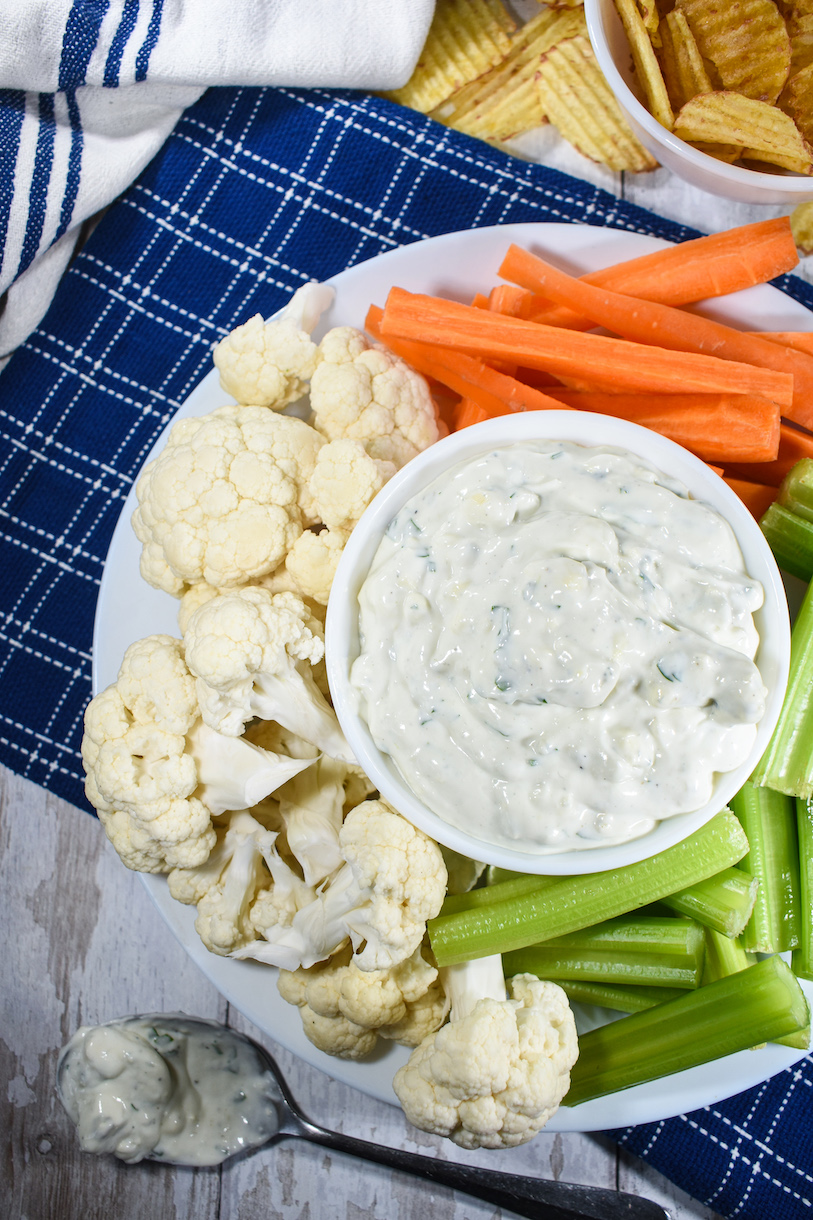 A bowl of blue cheese dip and plate of raw veg, arranged on a blue tea towel