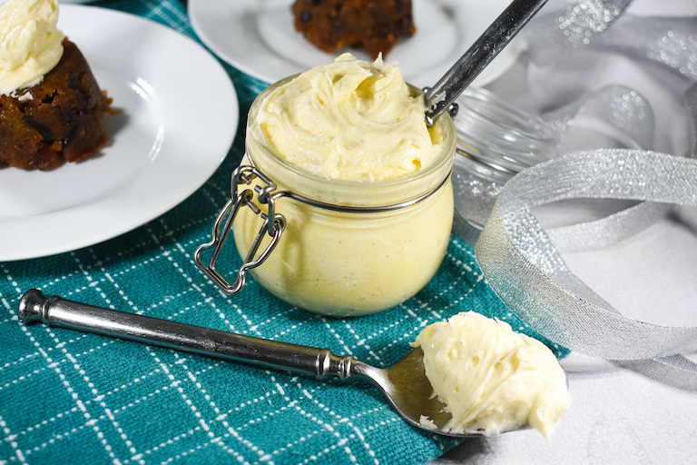 Christmas puddings, a spoon, and a glass jar of homemade brandy butter