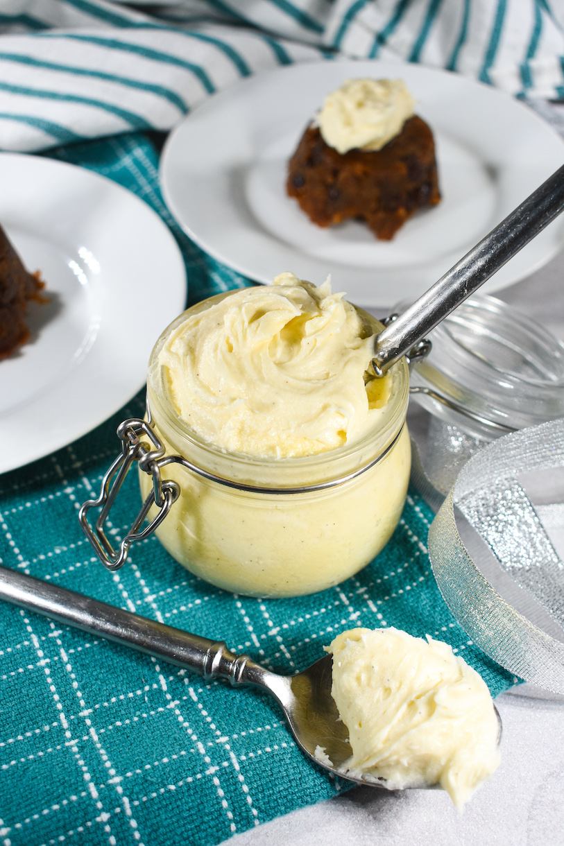 Christmas puddings, a spoon, and a glass jar of homemade brandy butter