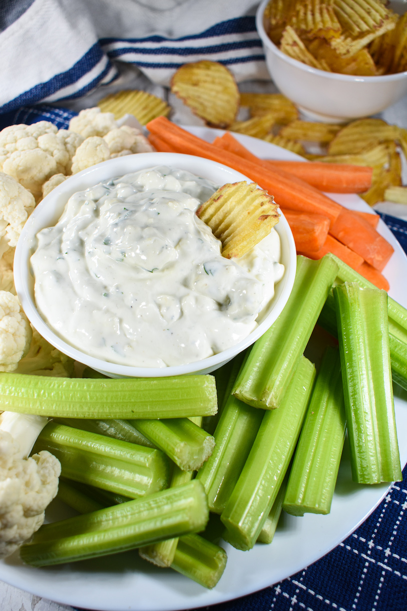 A chip dipped in blue cheese dip, with celery and carrot sticks and cauliflower florets