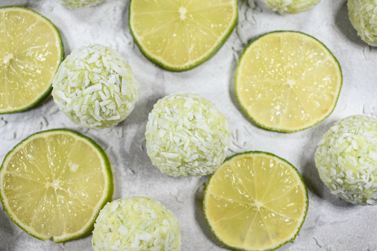 Coconut lime truffles and slices of lime on a white surface