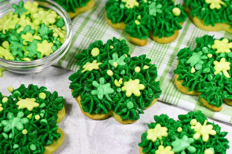 Saint Patrick's Day cookies, a bowl of sprinkles, and a green tea towel on a white surface