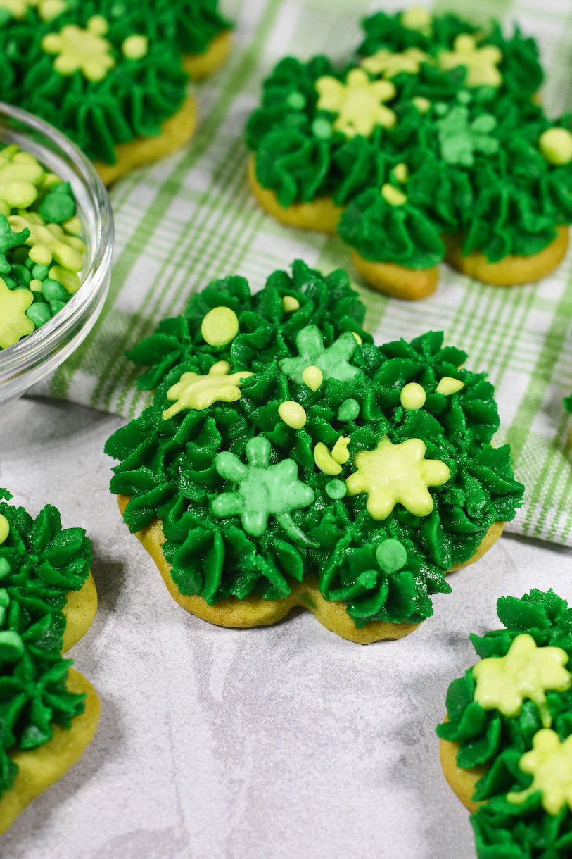 A green shamrock shaped cookie decorated with green buttercream and sprinkles for St. Patrick's Day