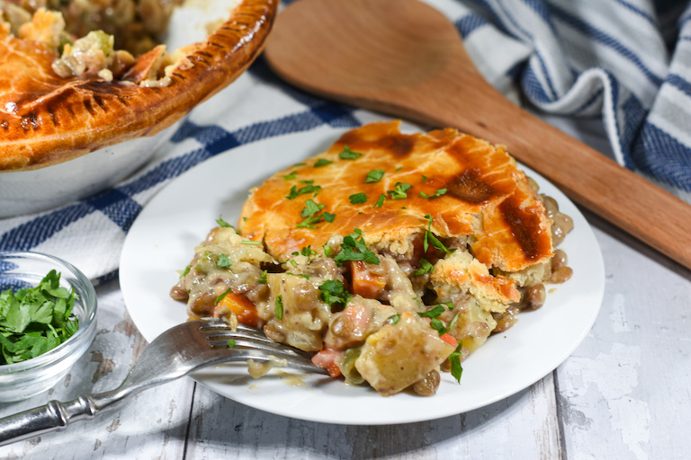 Vegetarian pot pie, blue plaid tea towel, and a wooden spoon on a white surface