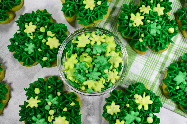 Looking down at a dish of shamrock sprinkles surrounded by green Saint Patrick's Day cookies