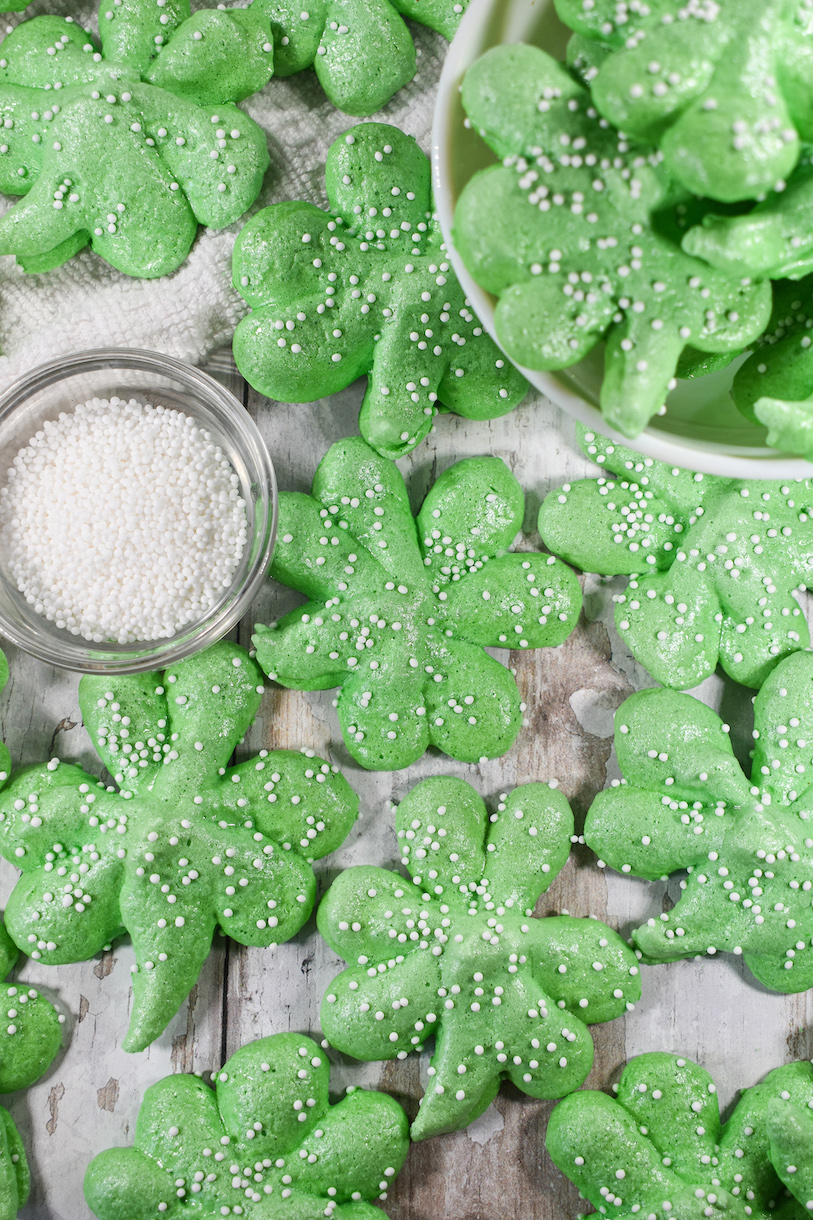 Shamrock meringues on a white surface with bowl of nonpareils