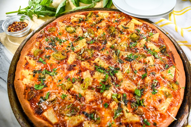 Horizontal shot of a jalapeño pizza with pineapples, mozzarella, and fresh herbs