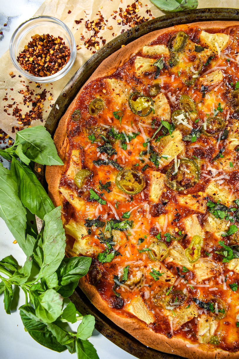 Jalapeno and pineapple pizza, fresh basil, and a bowl of chili flakes