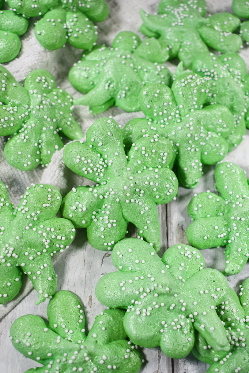 shamrock cookies and a dish of sprinkles on a white surface