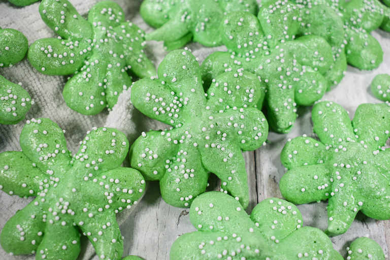 Green meringue shamrock cookies on a white surface