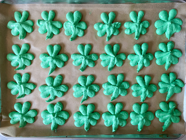 Meringue shamrock cookies piped on a parchment lined tray