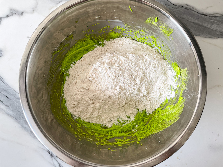 Adding dry ingredients to a bowl of green cookie dough