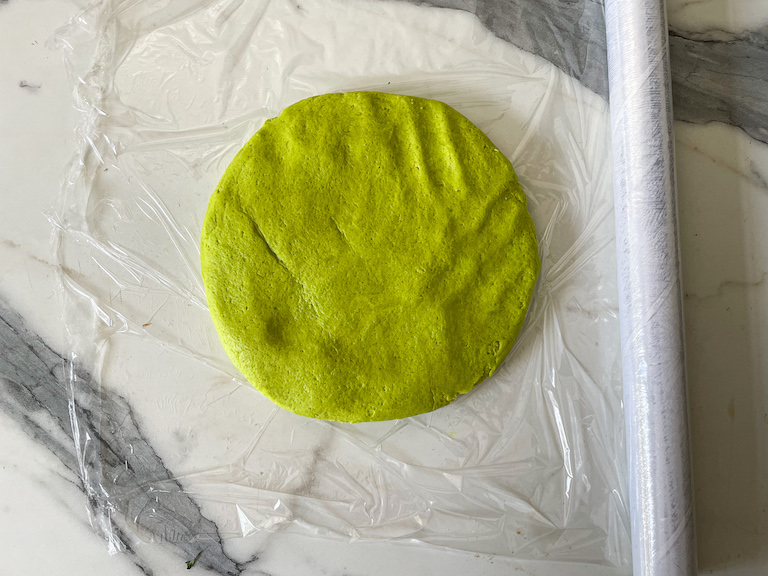 Disc of green dough on a sheet of plastic wrap