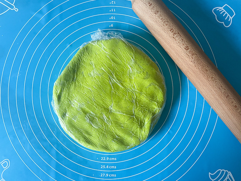 Green sugar cookie dough wrapped in plastic on a blue rolling mat