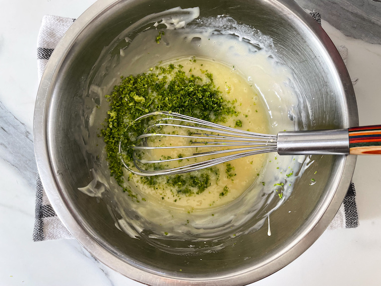 Adding lime zest to a bowl of melted white chocolate