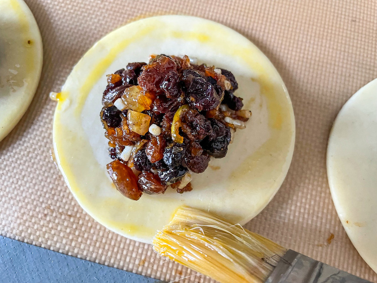 A pastry brush egg washing the edges of a mincemeat turnover