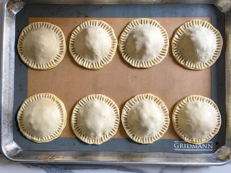 Round hand pies with fork crimped edges, arranged on a baking tray