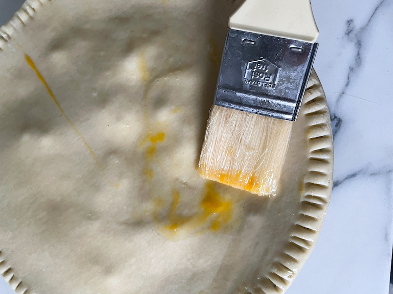 Pastry brush applying egg wash to top of unbaked pot pie