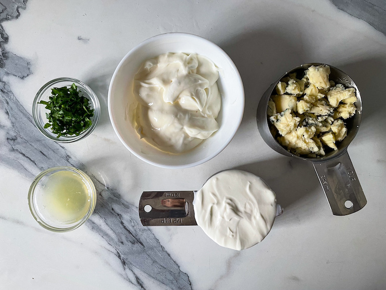 Ingredients for making this blue cheese dip recipe, arranged on a marble countertop