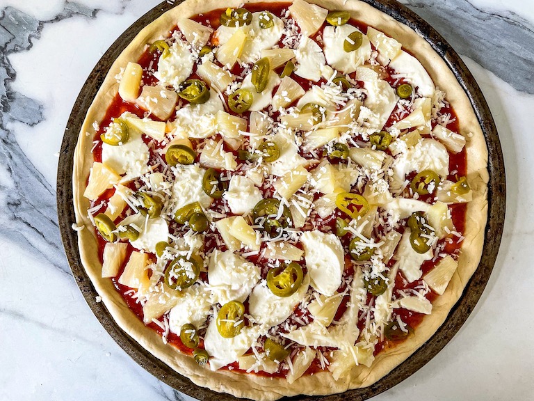 Parmesan scattered on pineapple pizza before baking