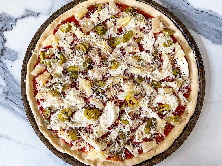 An unbaked jalapeno and pineapple pizza on a marble countertop