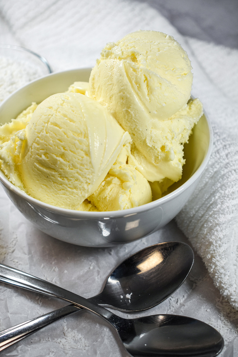 Scoops of homemade coconut ice cream in a white bowl with two spoons