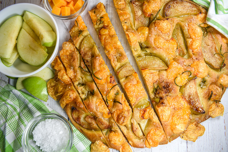 A loaf of cheddar focaccia with a bowl of apples and dish of sea salt