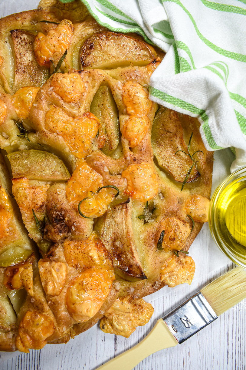 A loaf of apple cheddar focaccia with a pastry brush and dish of olive oil