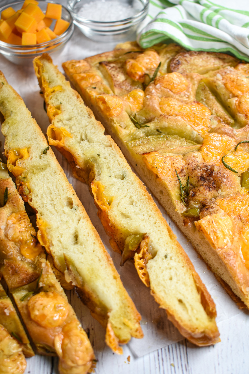 A loaf of cheddar focaccia with a bowl of apples and dish of sea salt