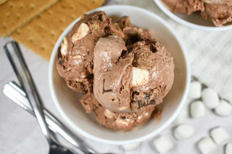 A dish of smores ice cream surrounded by graham crackers and marshmallows